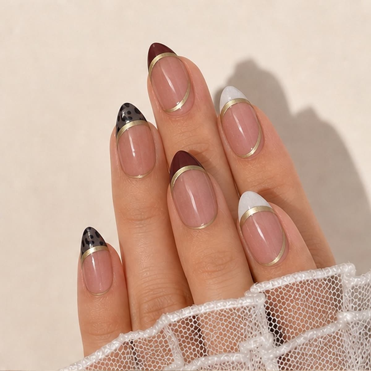 Duchesse brown, ivory and gold French press-on nails worn on a relaxed hand against a cream background