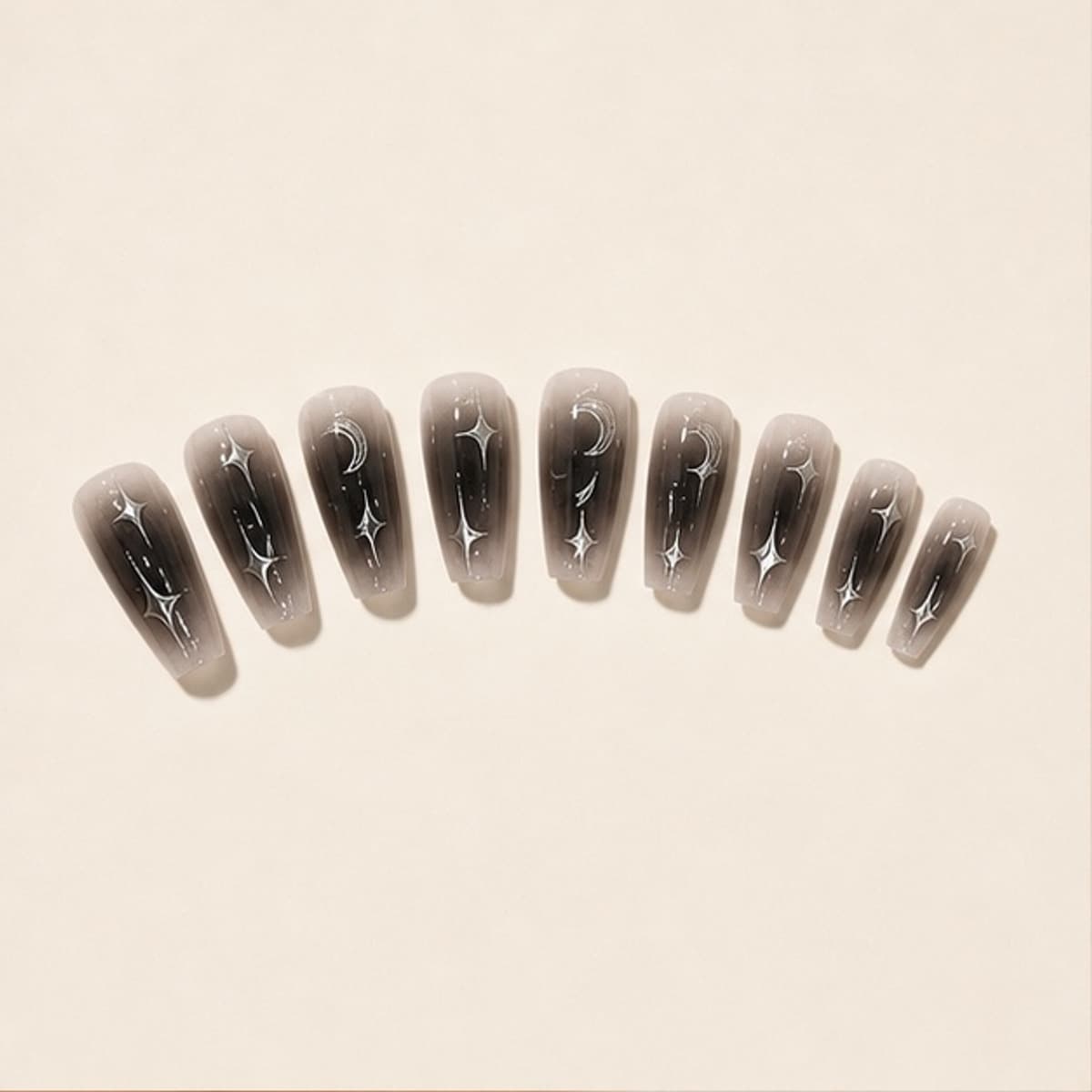 Nocturne black silver star press-on nail set arranged in a fan on an ivory background