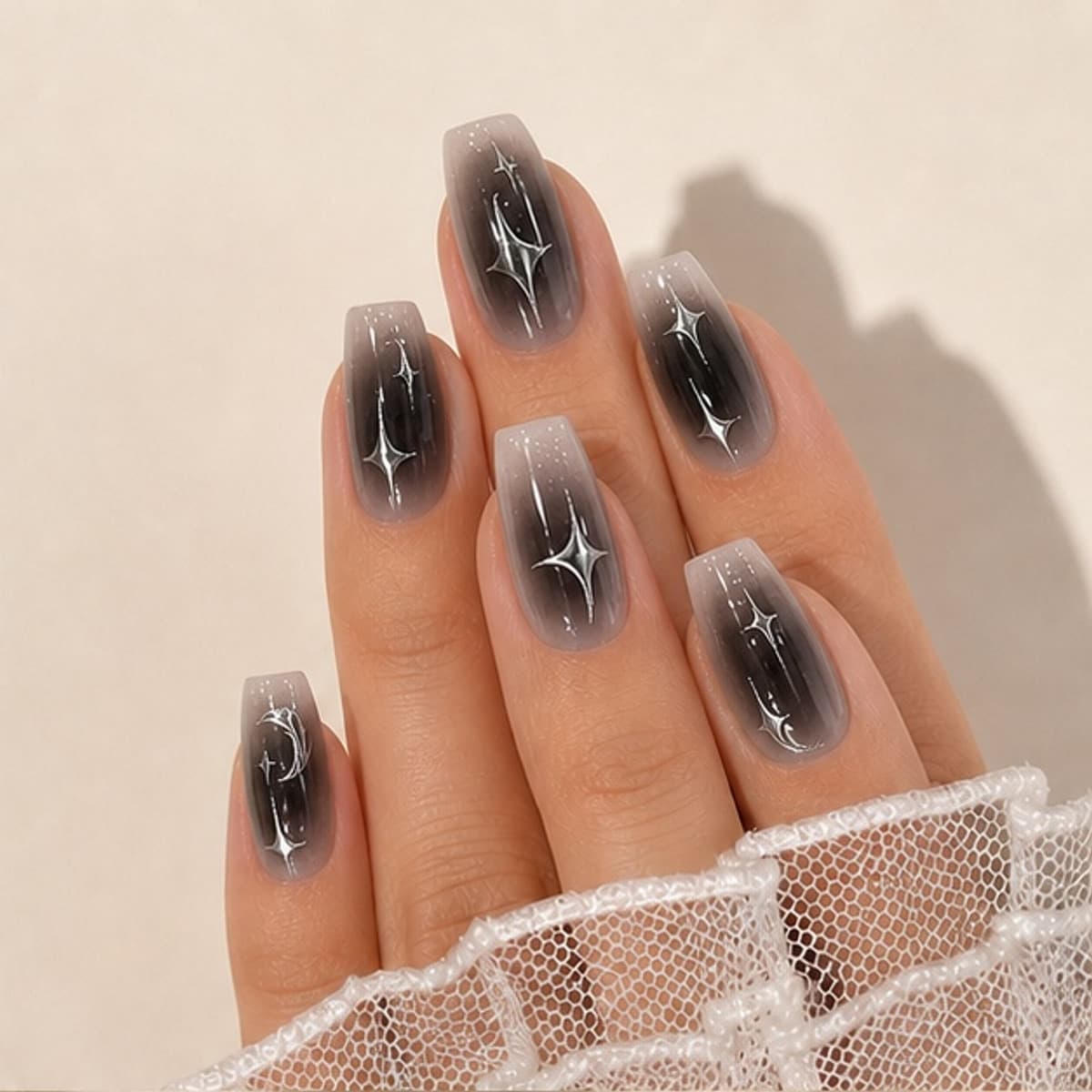 Nocturne black silver star press-on nails worn on a relaxed hand against a cream background