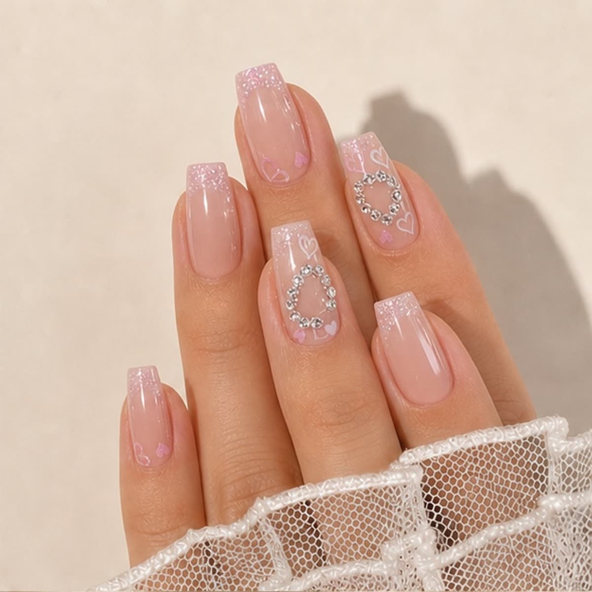 Perle crystal heart blush press-on nails worn on a relaxed hand against a cream background